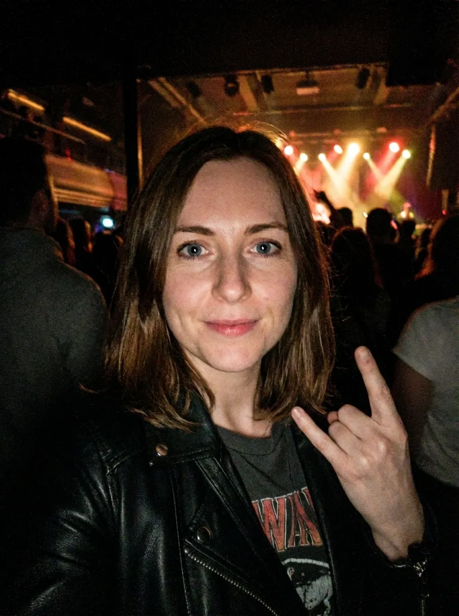 Original selfie input — woman in a dark jacket making a rock hand gesture at night